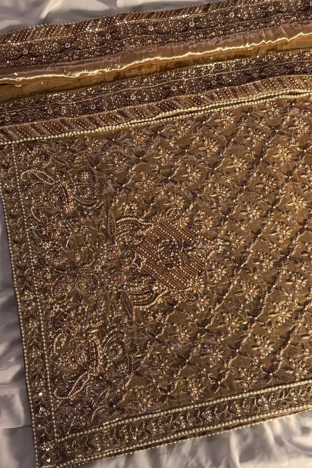 Close-up of a gold embroidered fabric with intricate patterns on a white background