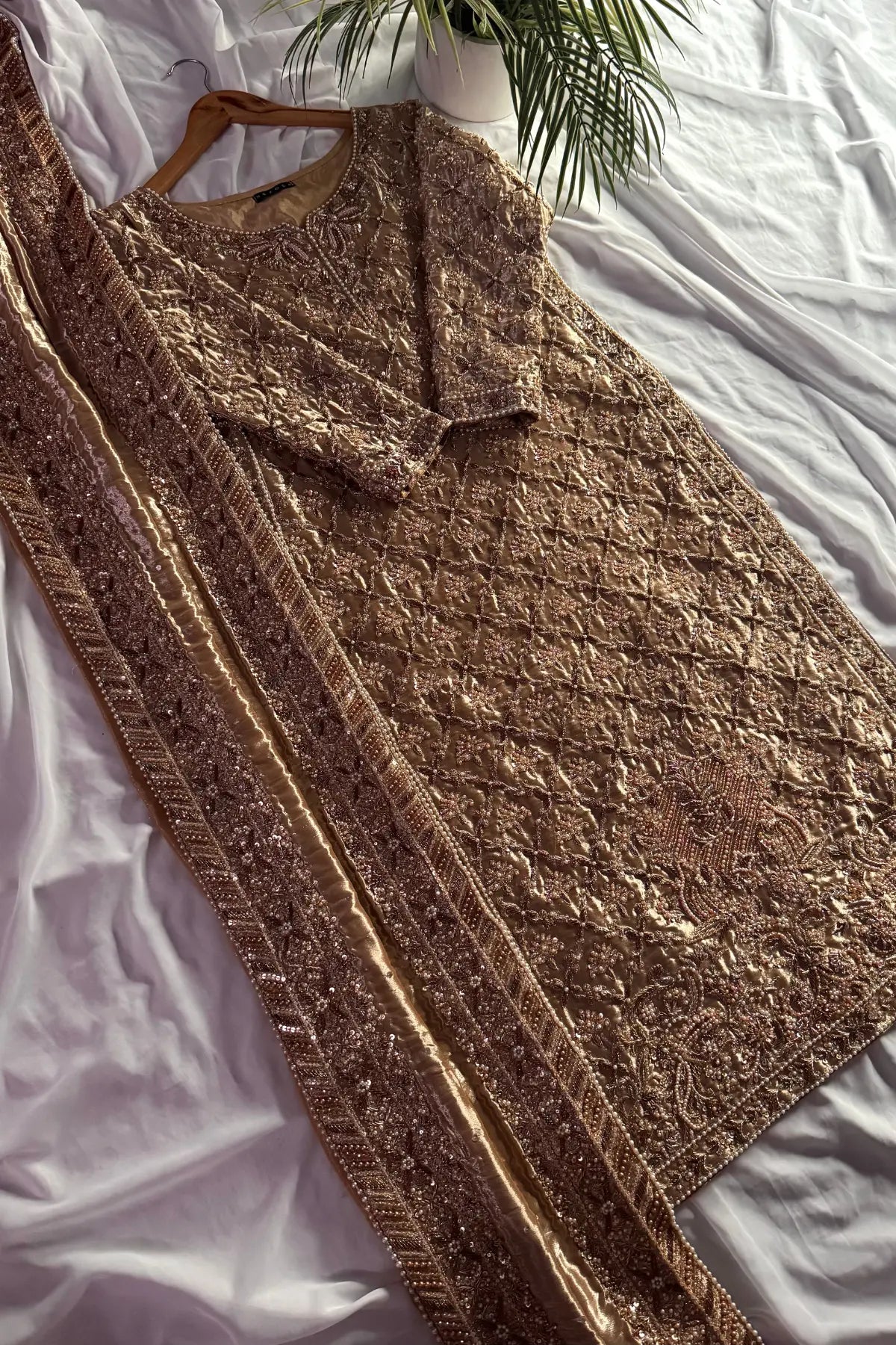 Brown knitted cardigan on a white surface with a plant in the background