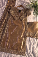 Gold embroidered traditional outfit on a white bed with a plant in the corner